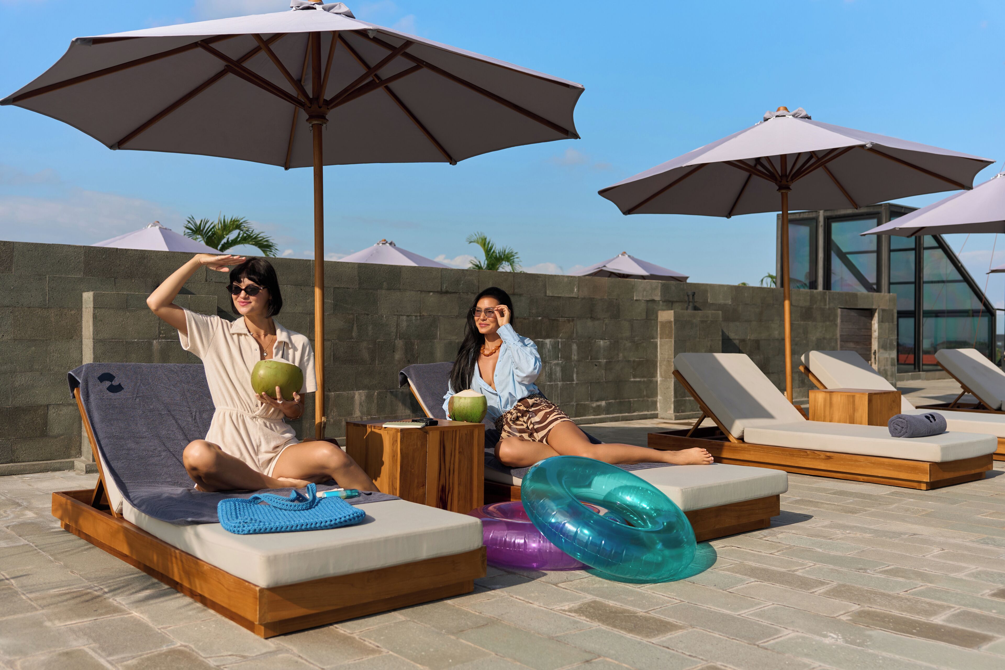 A poolside area with lounge chairs, umbrellas, and a stone wall in the background.