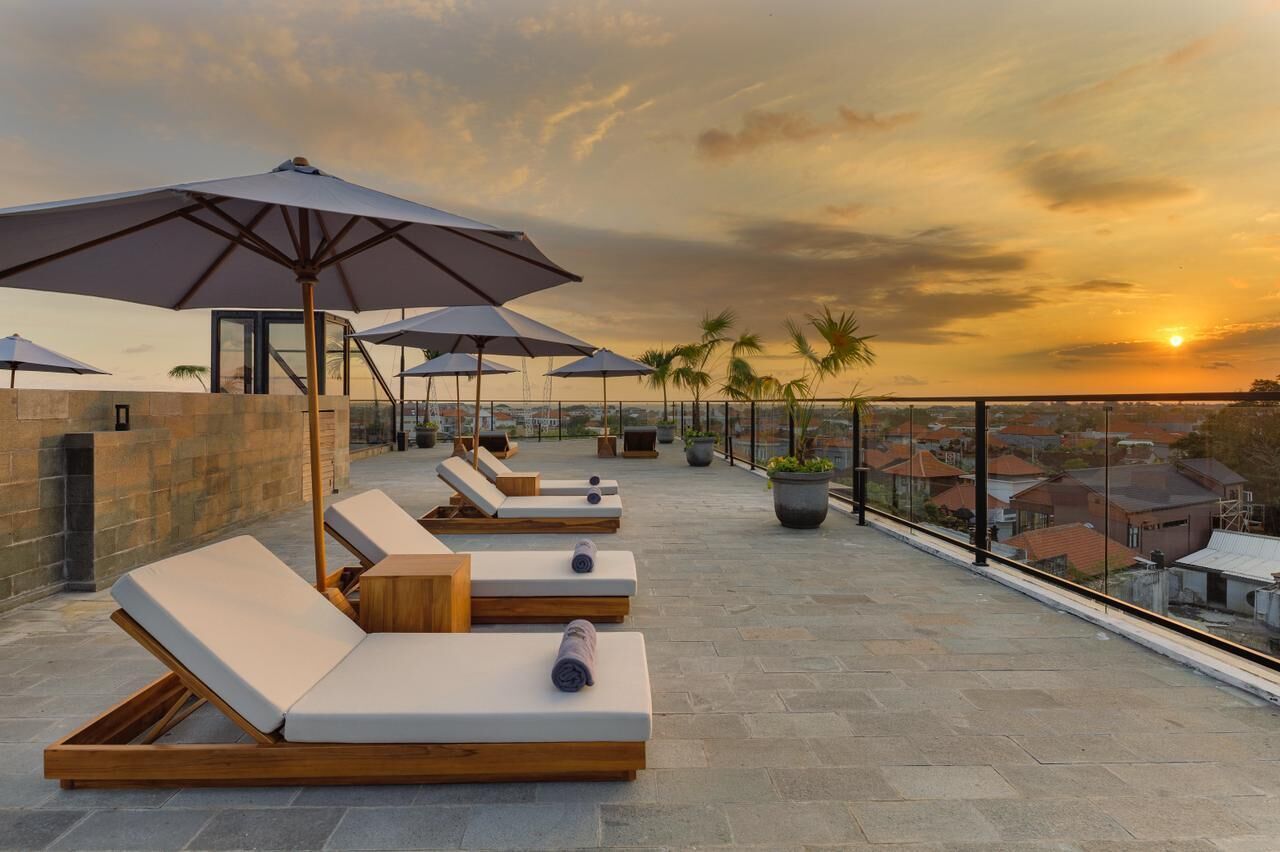 Eine Dachterrasse mit Liegestühlen, Sonnenschirmen und Blick auf den Sonnenuntergang über einem Wohngebiet.