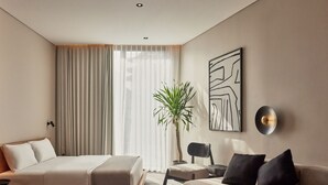 Et moderne hotelværelse med seng, sofa, stol, en potteplante og en vægmonteret lampe.