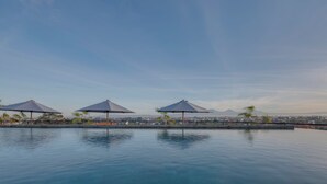 En pool med tre parasoller, en klar himmel og en by silhuet i det fjerne.