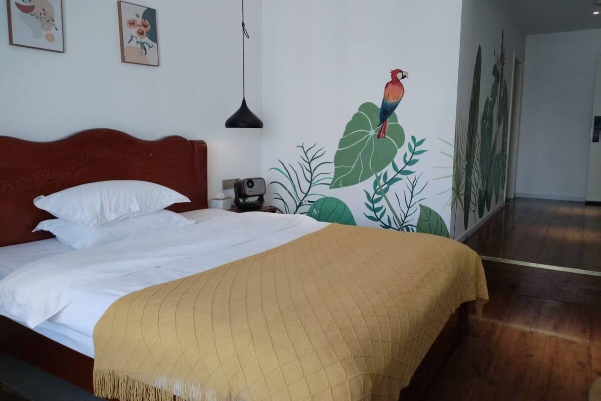 Habitación de hotel con una cama, una mesita de noche, una lámpara y un mural en la pared.