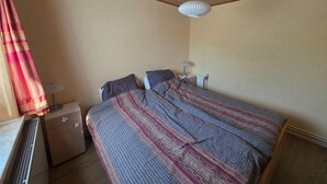 A bedroom with a bed, a nightstand, a lamp, and a radiator. - Bungalow for 6 Persons With a Very Spacious South-facing Garden (De Koog)
