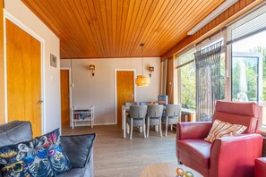 A room with a wooden ceiling, a dining area with chairs and a table, and a red leather sofa. - Bungalow for 6 Persons With a Very Spacious South-facing Garden (De Koog)