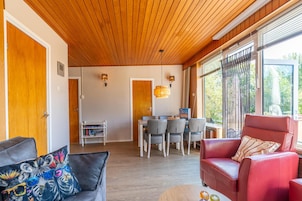 Et værelse med træloft, et spiseområde med stole og et bord, samt en rød lædersofa.