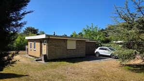 A small brick building with a garage, a car parked inside, and a clear blue sky. - Bungalow for 6 Persons With a Very Spacious South-facing Garden (De Koog)