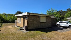 A small brick building with a garage, a car parked in front, and a clear blue sky. - Bungalow for 6 Persons With a Very Spacious South-facing Garden (De Koog)