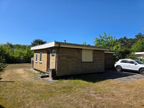 A small brick building with a garage, a car parked in front, and a clear blue sky. - Bungalow for 6 Persons With a Very Spacious South-facing Garden (De Koog)