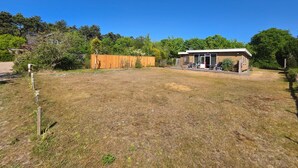 A small house with a patio, surrounded by a fenced yard and trees. - Bungalow for 6 Persons With a Very Spacious South-facing Garden (De Koog)