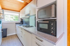 A compact kitchen with white cabinets, a gas stove, a microwave, and a window with a view of greenery. - Bungalow for 6 Persons With a Very Spacious South-facing Garden (De Koog)