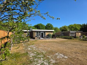 A two-story building with a patio area, a fenced yard, and a wooden fence. - Bungalow for 6 Persons With a Very Spacious South-facing Garden (De Koog)