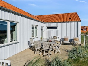 En hvid bygning med rødt tegltag, træterrasse og udendørs møbler.