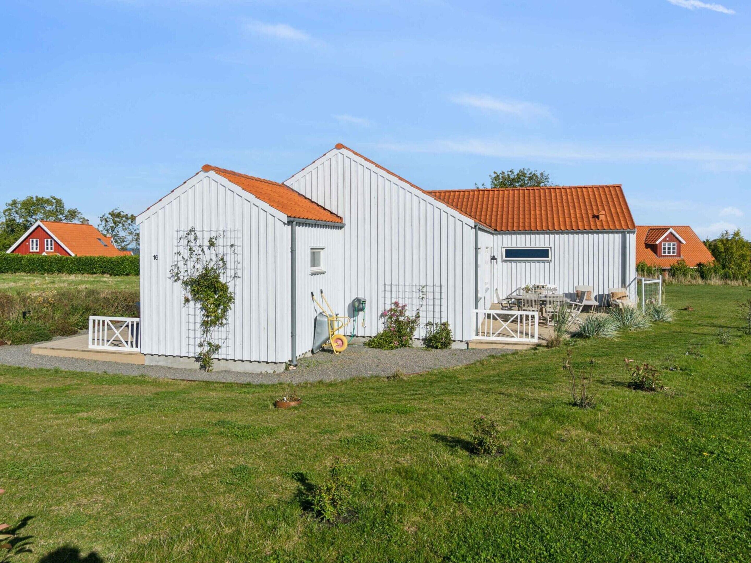 A white barn with a red roof and a small attached structure with a white fence.