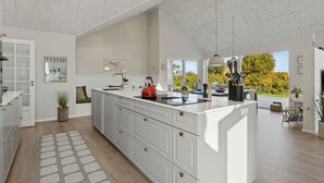 A spacious kitchen with a large island, white cabinetry, and a view of the outdoors. - 4 Star Holiday Home in Svaneke (Svaneke)