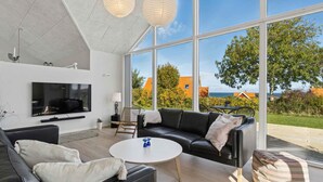 A modern living room with a large TV, black leather sofa, and a round coffee table. - 4 Star Holiday Home in Svaneke (Svaneke)