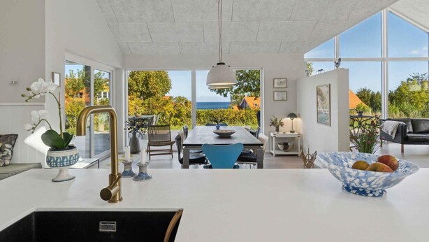 A modern kitchen with a large island, a dining area with a view, and a living space with a sofa and a table. - 4 Star Holiday Home in Svaneke (Svaneke)
