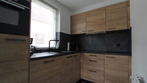 A kitchen with wooden cabinets, a black countertop, and a window with blinds. - Modern Bungalow in Ewijk for 6 (Ewijk)