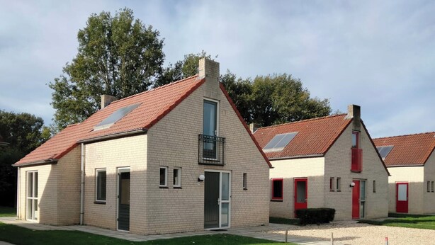 A row of two-story buildings with red-tiled roofs, a grassy lawn, and a gravel path. - Modern Bungalow in Ewijk for 6 (Ewijk)