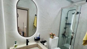 Un bagno moderno con uno specchio ovale grande, un mobile bagno color beige, un water bianco e una cabina doccia in vetro.