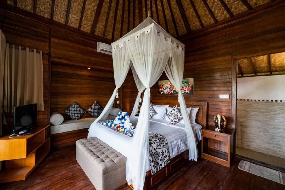 Una habitación de madera con una cama con dosel, un televisor sobre un atril de madera, y un banco acolchado.
