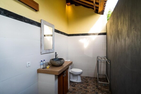 Ein Badezimmer mit einem Holzbadezimmer, einem runden Waschbecken, einer weißen Toilette und einem Metallregal.