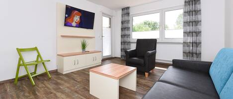 A modern living room with a sofa, a coffee table, a chair, a TV, and a kitchen area.