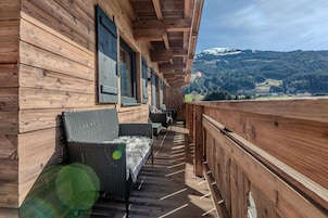 Ein Holzbalkon mit Korbmöbeln und Blick auf eine Berglandschaft.