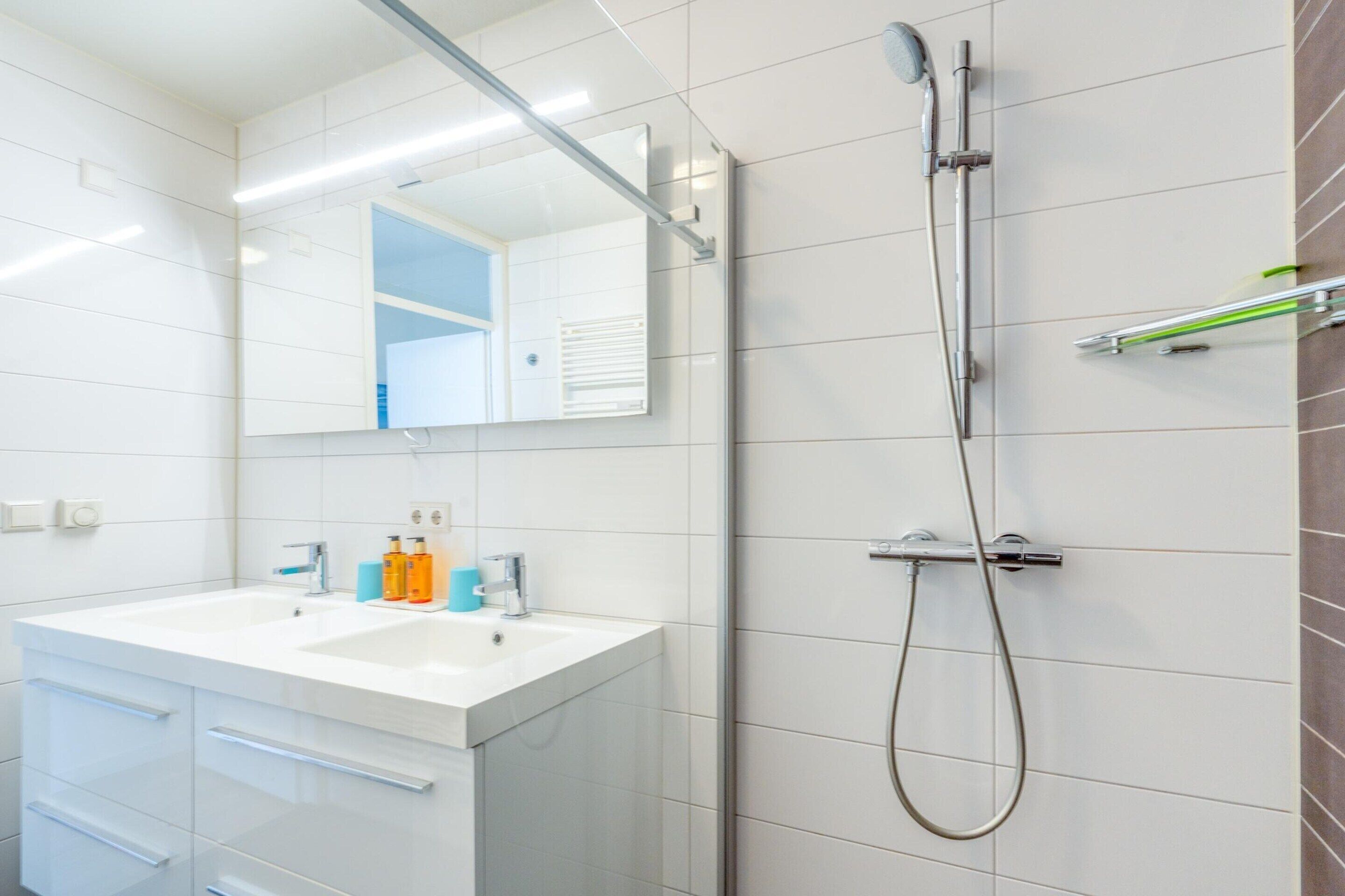 A modern bathroom with a white vanity, a large mirror, a shower with a handheld showerhead, and a towel rack.