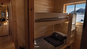 Una cabaña de madera con literas, una ventana con vistas a montañas y un escritorio pequeño con una silla.