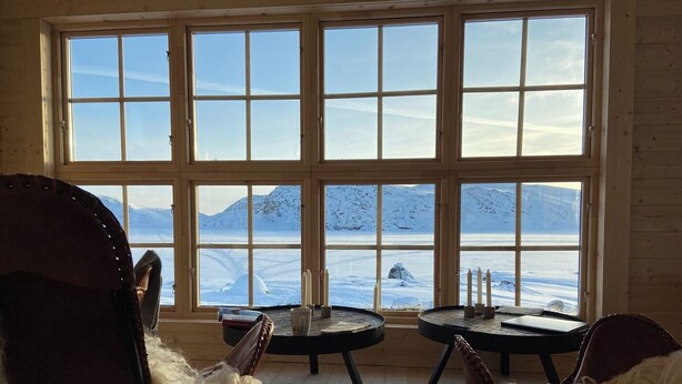 Una habitación con ventanas amplias que ofrecen vistas a un paisaje nevado. Hay dos sillones con mantas de piel, una mesita y un candelabro.