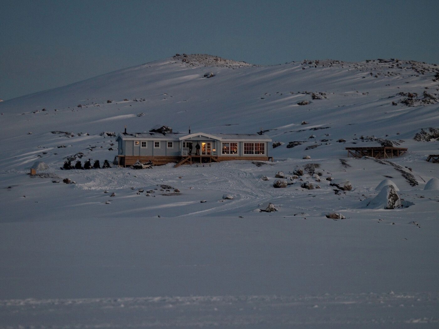 A snow-covered landscape with a single building featuring a large windowed front and a smaller structure nearby.