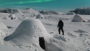 Paisaje nevado con iglúes y una persona de pie a lo lejos.