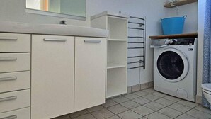 A compact, modern bathroom with a built-in sink, a mirror, a washing machine, and a drying rack.