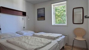 A simple, clean room with two beds, a window with a view of greenery, a chair, and a poster on the wall.
