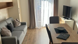Una sala moderna con un sofá gris, una mesa de comedor de madera y un televisor sobre un mueble bajo.