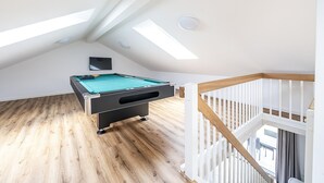 Une table de billard dans une pièce au plancher en bois et au plafond incliné, percé de lucarnes.