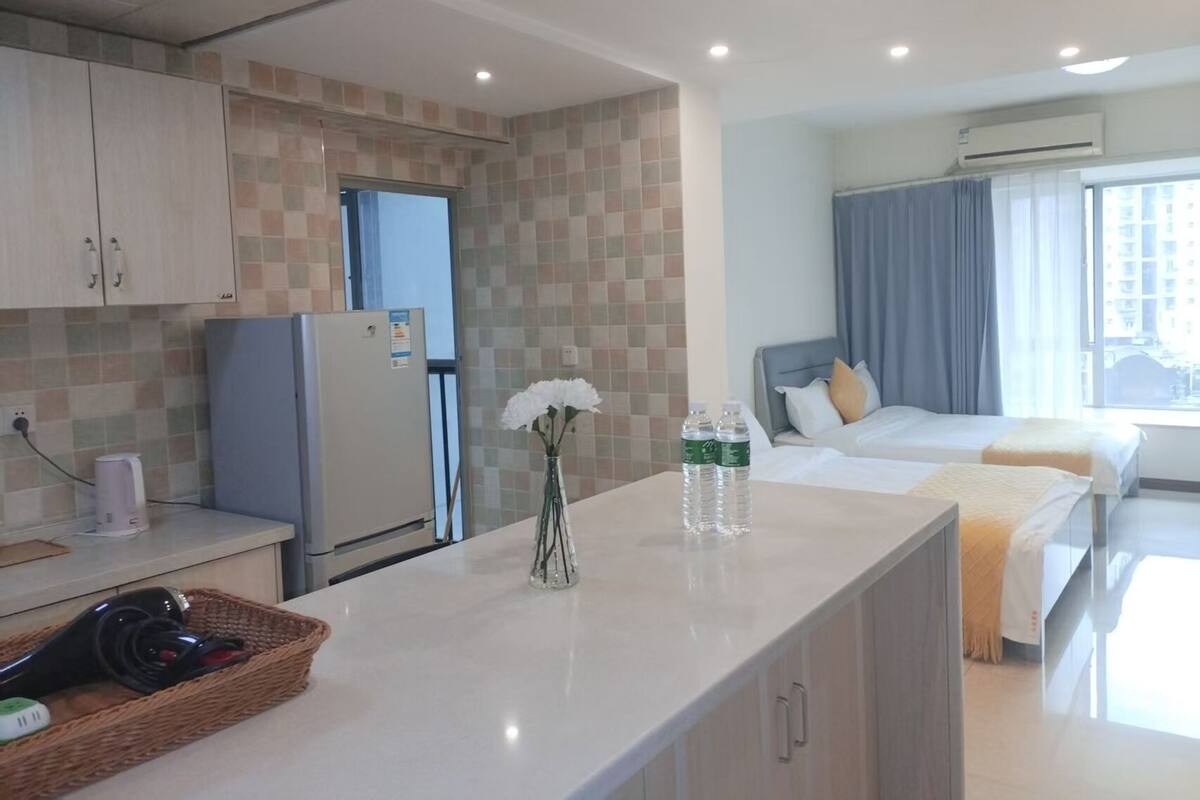 A modern hotel room with a kitchenette, a bed with a view, and a bathroom with a shower and toilet.