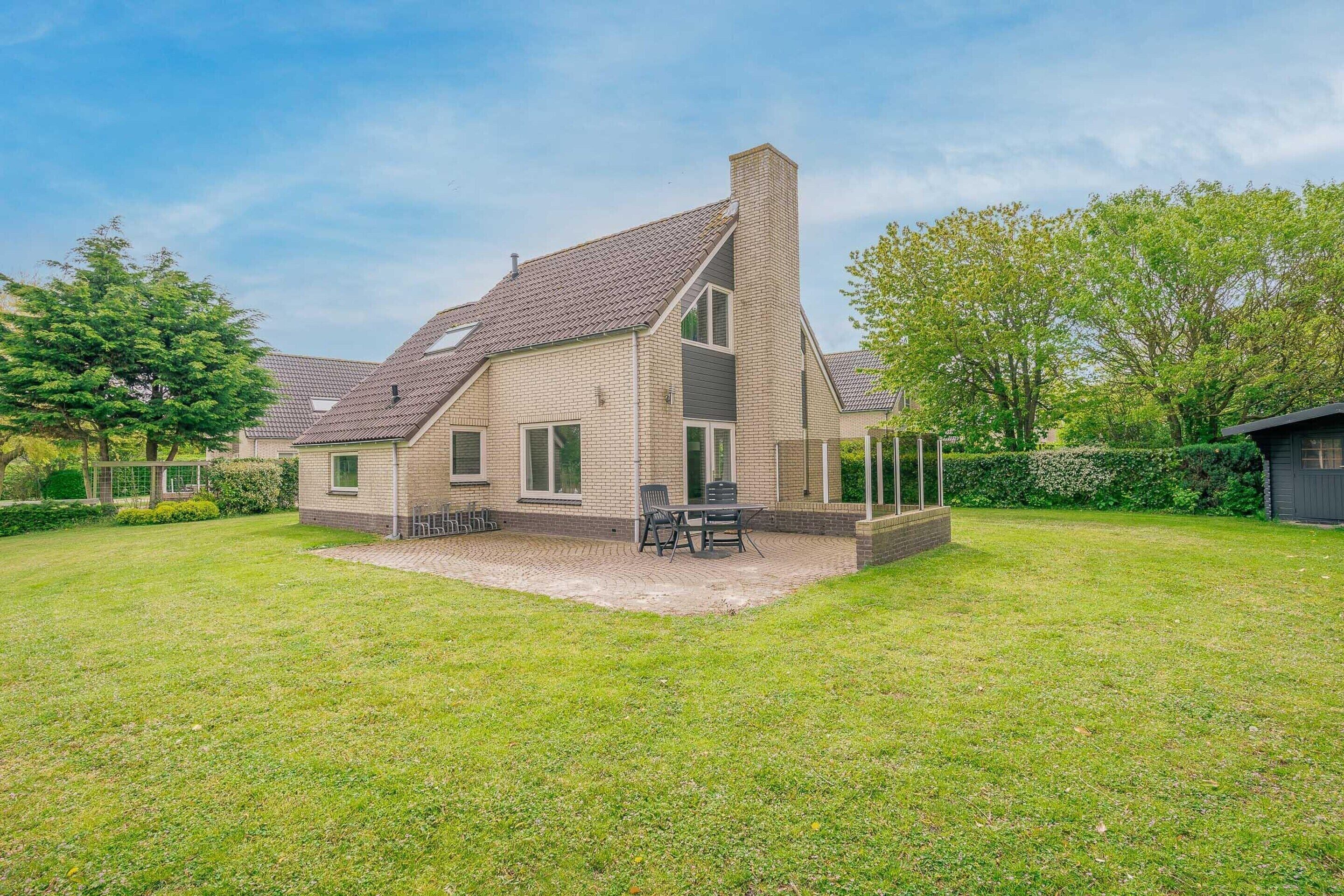 A two-story house with a sloped roof, a chimney, and a covered patio area with outdoor furniture.