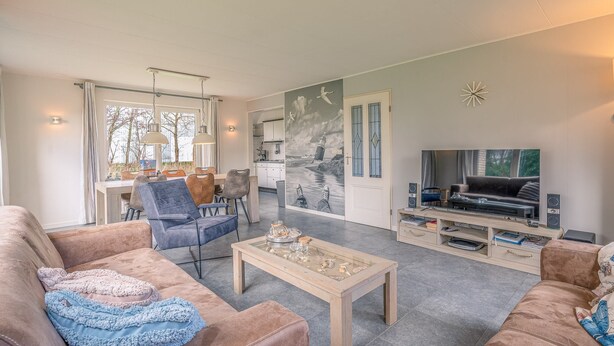 Een woonkamer met een bank, salontafel, televisie en een eethoek met stoelen en een tafel.