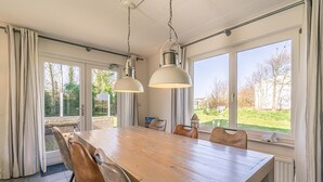Een ruime eethoek met een grote houten tafel en lederen stoelen, grote ramen met gordijnen en hanglampen.
