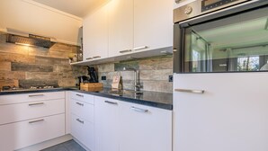 Een moderne keuken met witte kasten, een roestvrijstalen afzuigkap, een inbouwoven en een groot raam.