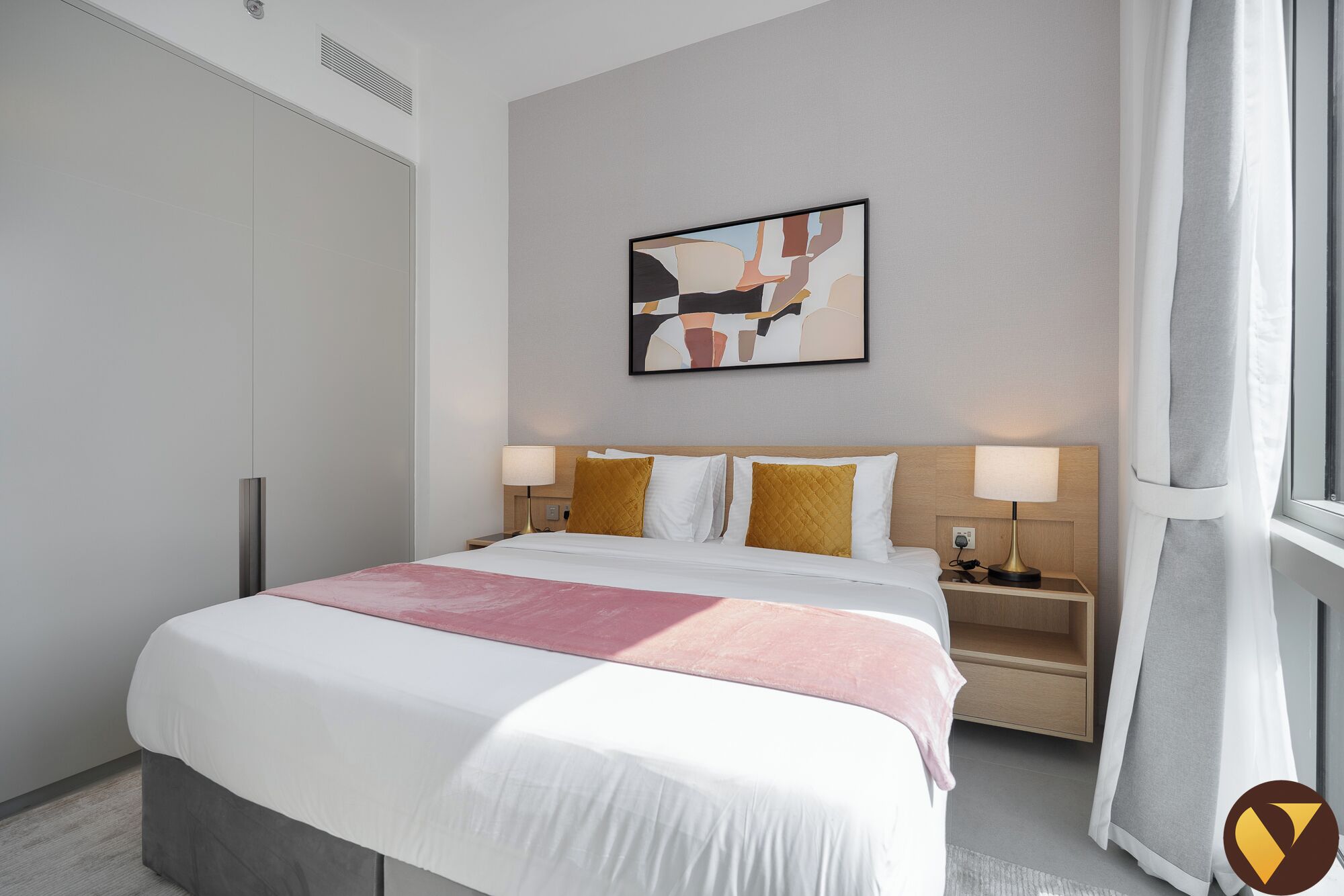 Una camera d'albergo con un letto, due comodini, un quadro astratto appeso al muro e una finestra con tende.