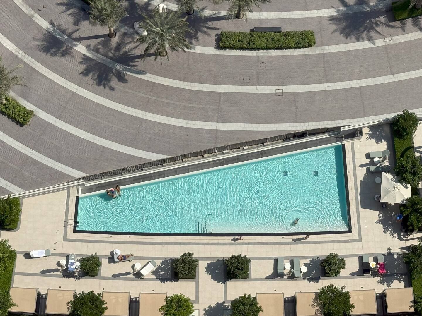 An aerial view of a swimming pool with surrounding lounge areas and palm trees.
