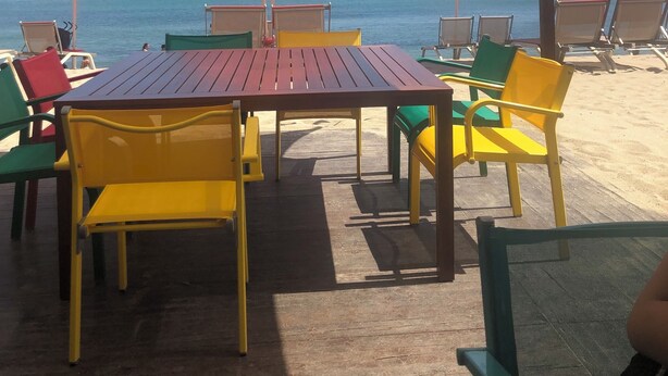 A beachside café with outdoor seating, including tables and chairs, under a canopy.