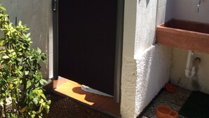 A small outdoor bathroom with a closed door, a tiled sink, and a small plant.