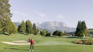 A golf course with a player preparing to putt, surrounded by trees and mountains in the background. - Apartment With ski Lift Right Outside the Door (Jochberg)