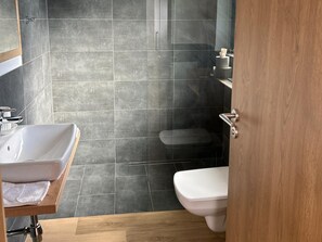 Un baño moderno con un lavamanos blanco, un inodoro y una zona de ducha.