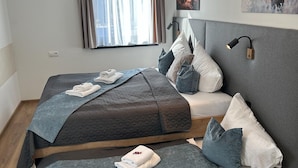 A modern bedroom with two beds, a bedside table, a lamp, and a window with curtains. - Apartment With ski Lift Right Outside the Door (Jochberg)