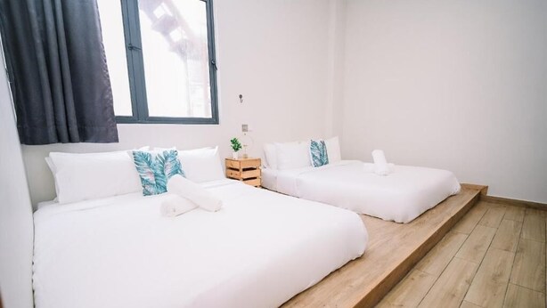 Une chambre d’hôtel avec deux lits, du linge de lit blanc, une plateforme en bois, une petite table de chevet avec une plante et une fenêtre avec des rideaux.