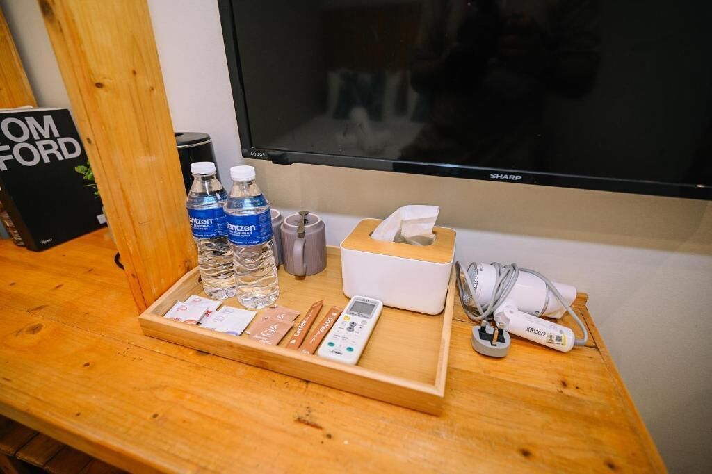Sur une table, on trouve un plateau en bois avec des bouteilles d’eau, une boîte de mouchoirs, une télécommande et une multiprise.