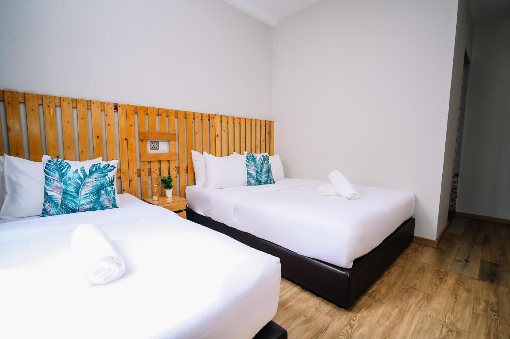 Habitación de hotel con dos camas, cabecero de madera, ropa de cama blanca y una pequeña planta en maceta.